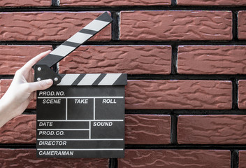 Clapper plates, women's hands and a movie clapper with a brick background