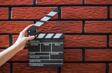 Clapper plates, women's hands and a movie clapper with a brick background