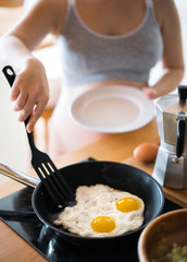 Two fried eggs in a saucepan with olive oil. Girl's hand with a plate of frying pan with fried eggs in the morning.