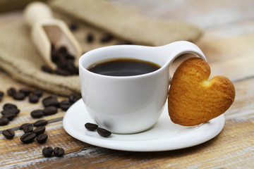 Heart shaped cookie leaning against cup of coffee on rustic wooden surface
