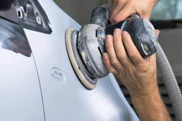 Grinder in the hands of a man who sharpen a car varnish in the car shop.