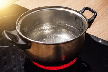 Metal pan with boiling water on the induction cooker red hot plate.
