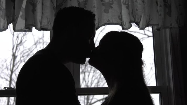 pregnant couple kiss forehead to forehead cute backlit window close up 4k