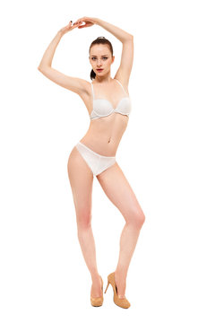 The girl is standing with her hands up. A fashion model posing in her underwear. Isolated on white background.