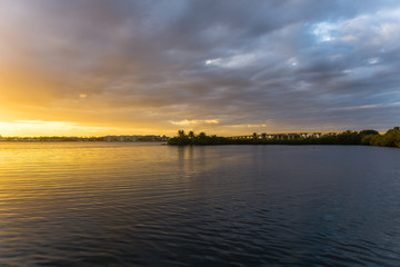 Fototapeta premium USA, Florida, Orange glowing sky with some clouds and highway bridge behind reflecting water