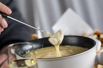 Mann isst klassisches Käse Fondue mit Brot und Sekt