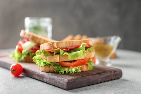 Wooden board with delicious sandwich on table, closeup