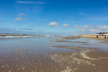 Beach view with dunes and waves at Bergen aan Zee, northern Holland. The sun is shining bright from a blue sky on a sunny day.