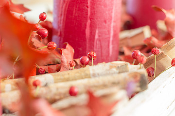christmas wreath decoration with red dried rosehip berries, on a modern christmas wreath with four candles. Wood pieces, red candles and red oak tree leaves are put besides on this christmas wreath.