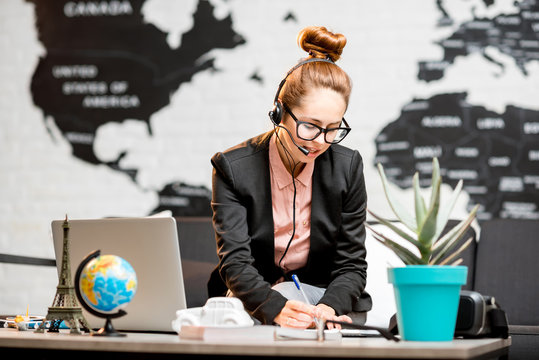 Portrait of a female travel agent in the suit and headset working indoors on the world map background