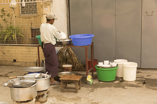 Hombre fregando los platos de un restaurante en la calle. Asia.
