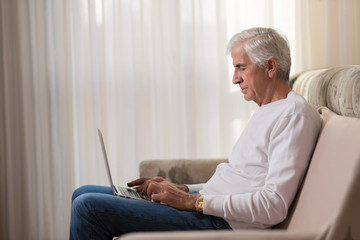 Senior man using laptop at home and surfing the net