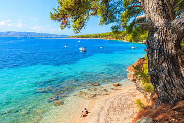 Fototapeta premium Unidentified couple of people sitting on beach near famous cape Zlatni Rat in Bol town, Brac island, Croatia