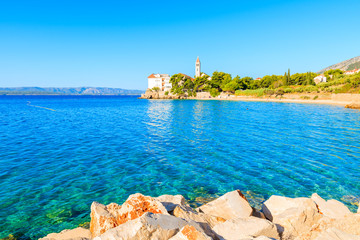 Fototapeta premium Rocks and beautiful sea water with Dominican monastery in distance, Bol town, Brac island, Croatia