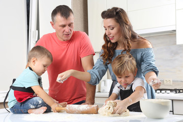 young parents next to small children who knead the dough on the kitchen table