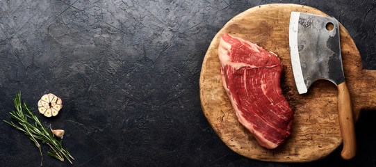 Raw fresh marbled meat Black Angus steak and meat cleaver on wooden board. Meat on black background...