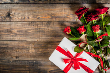 Fototapeta na wymiar Holiday background, Valentine's day. Bouquet of red roses, tie with a red ribbon, with wrapped gift box. On wooden table, copy space top view