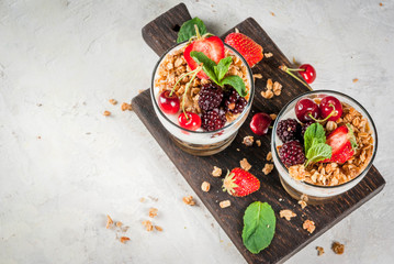 Healthy breakfast. Summer berries and fruits. Homemade Greek yoghurt with granola, blackberries, strawberries, cherries and mint. On white concrete stone table, in glasses. Copy space top view