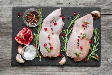 Raw chicken legs with herbs, spices and pomegranate on dark slate cutting board
