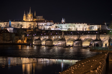 Fototapeta na wymiar A night photo of Prague with reflections in water. In view Illuminated Charles bridge in foreground, historic skyline of Lesser Side and Prague castle on the hill above the Vltava (Moldau) river.