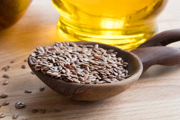 Linseed on a wooden spoon, with flaxseed oil in the background