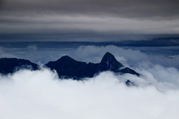 Fototapeta na wymiar Sharp peaks of Carnic Alps main ridge rise above low level clouds in overcast summer evening, Cima Avostanis Blaustein, Creta di Timau Hocheck, Friuli Venezia Giulia Italy / Carinthia Austria Europe