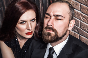 Passion concept, closeup. Bearded man closed eyes, redhead sensual woman with red lips and handsome makeup, looking at camera