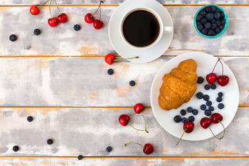 Top view of a delicious breakfast with croissants, coffee and blueberries and cherry on the table.