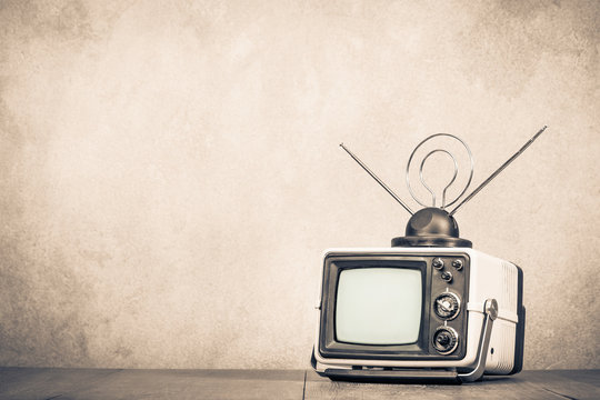 Retro old TV set receiver on table front textured concrete wall background. Television broadcasting concept. Vintage style sepia photo