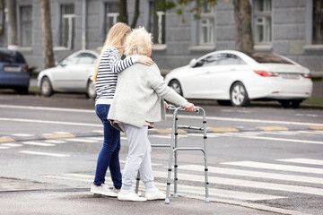 Young woman helping her elderly grandmother with walking frame to cross the road