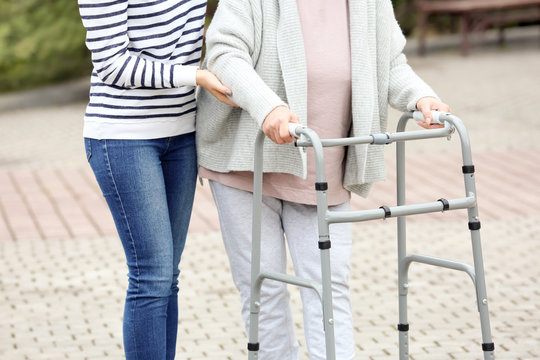 Young woman and her elderly grandmother with walking frame outdoors