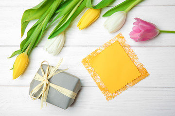Tulips, empty card and gift box on wooden background, top view