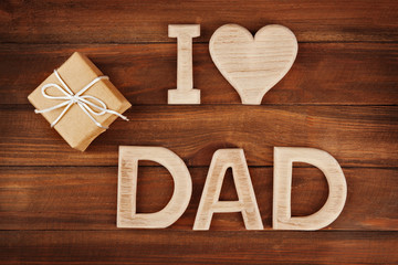 Greeting for Father's day with phrase "I LOVE DAD" made of letters and gift box on wooden background