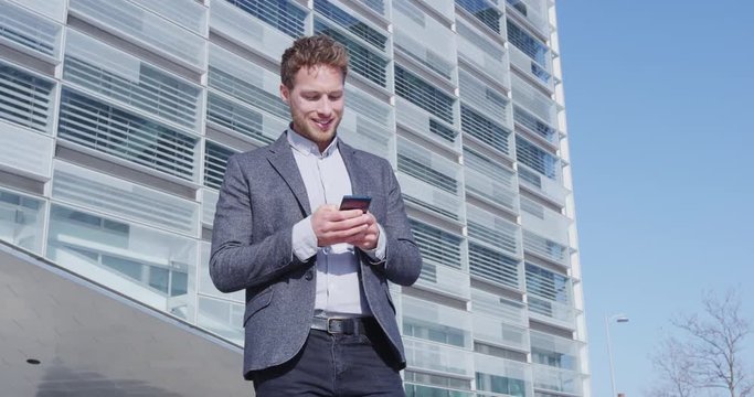 Phone - young businessman using smartphone in smart casual suit by office in city. Urban business man professional outside using mobile phone app outdoors confident in blazer. RED EPIC SLOW MOTION.