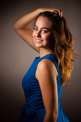 Fototapeta premium Portrait of beautiful young caucasian woman in blue dress over dark gray background