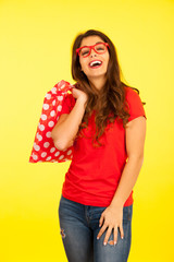 Beautiful young woman with shopping bags over vibrant yellow background