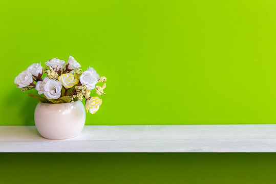 Green Wall With Flowers On Shelf White Wood, Copy Space For Test. Still Life Concept