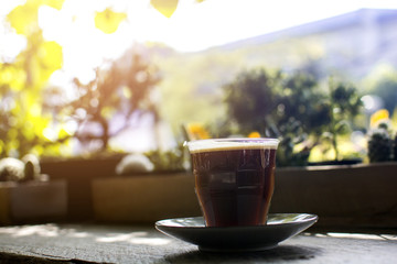 Glass of hot Americano with steaming on a wooden table in the cafe with bokeh tree garden background, black coffee.