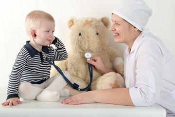 Happy cute boys playing with stethoscope in doctors office, hugging plush toy bear and smiling at camera. Female pediatrics. Copy space
