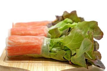 Salad roll in noodle with carrot and fresh vegetables on wooden plate and white background, heathy eating concept