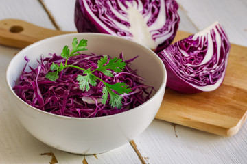 Cut or Sliced fresh purple cabbage in white bowl and decorate with coriander in side view on white wood table. Prepare vegetable for cooking cabbage salad or coleslaw. Homemade food concept.