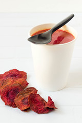 Beetroot soup in white paper cup with chips on white.