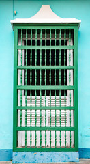 White shuttered window with green wooden bars on blue wall, newly painted