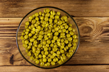 Canned green peas in glass bowl on wooden table