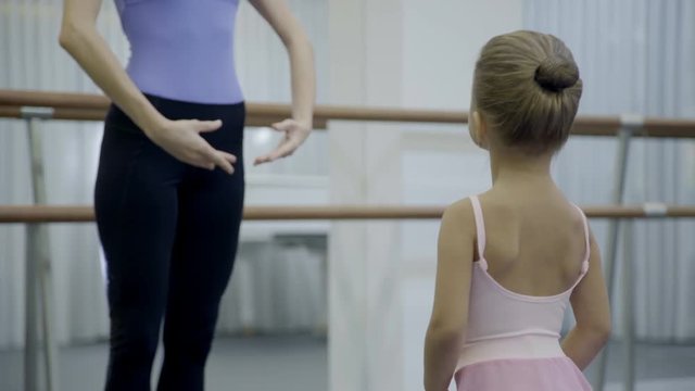 Female teacher teaches little girl in ballet school