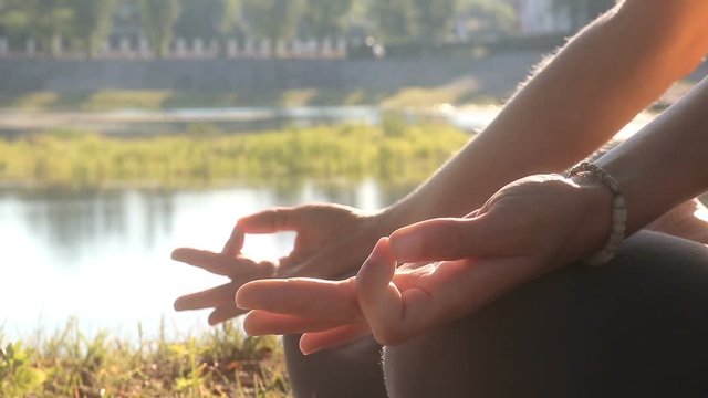 Young woman sits in lotus pose with hands jnana mudra in park outdoors. Female in padmasawa pose, arms are kneeling, thumb and forefinger are connected, forming circle. Serene lady dressed in gray