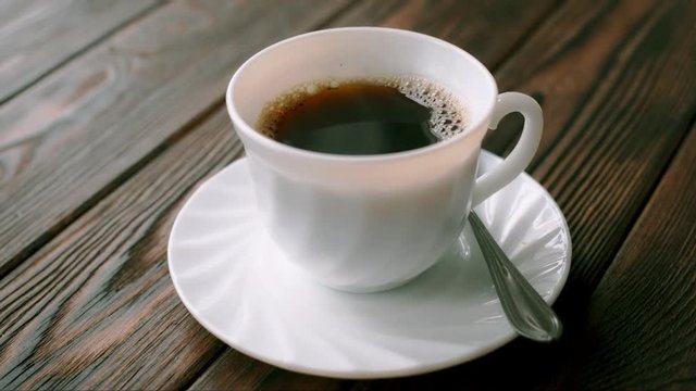 A cup of hot coffee stands on a wooden table
