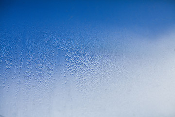 Water drops on a window glass on a blue cloudy sky background