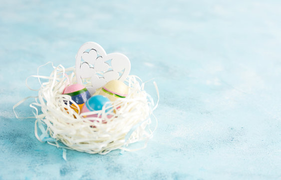 White paper nest with three vintage Easter eggs and wooden heart on blue background. Text space