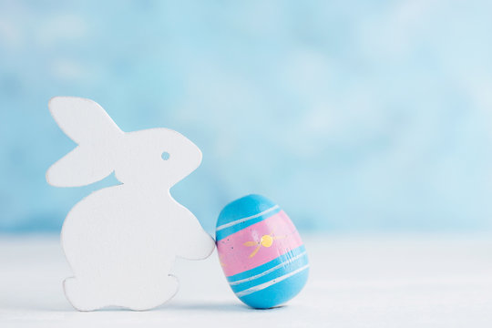 Bright Easter background: white wooden bunny with paited egg against blue wall. Holiday concept. Text space